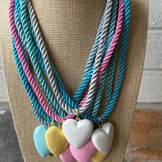 Necklace with colorful heart pendants on a mannequin bust against a textured wall.